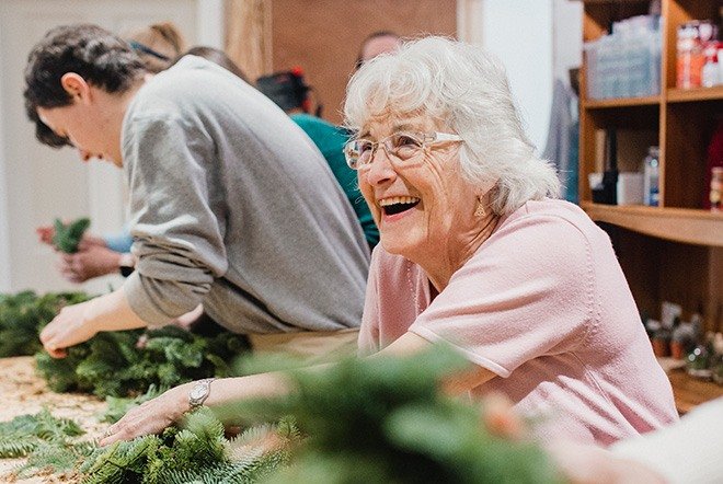 an elderly woman smiling while making christmas crafts