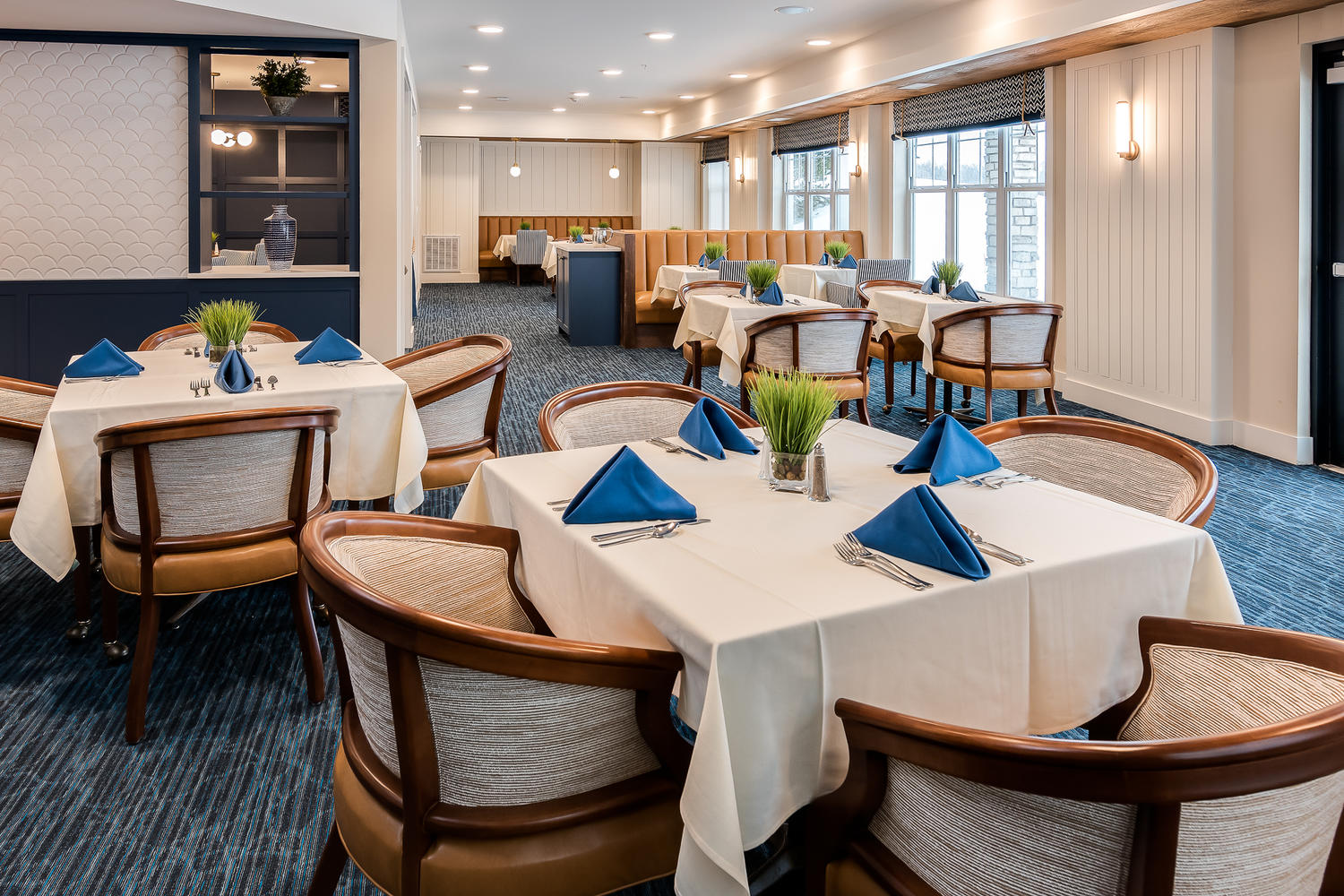 A few tables with white tablecloths, blue napkins, and silverware on top of them.