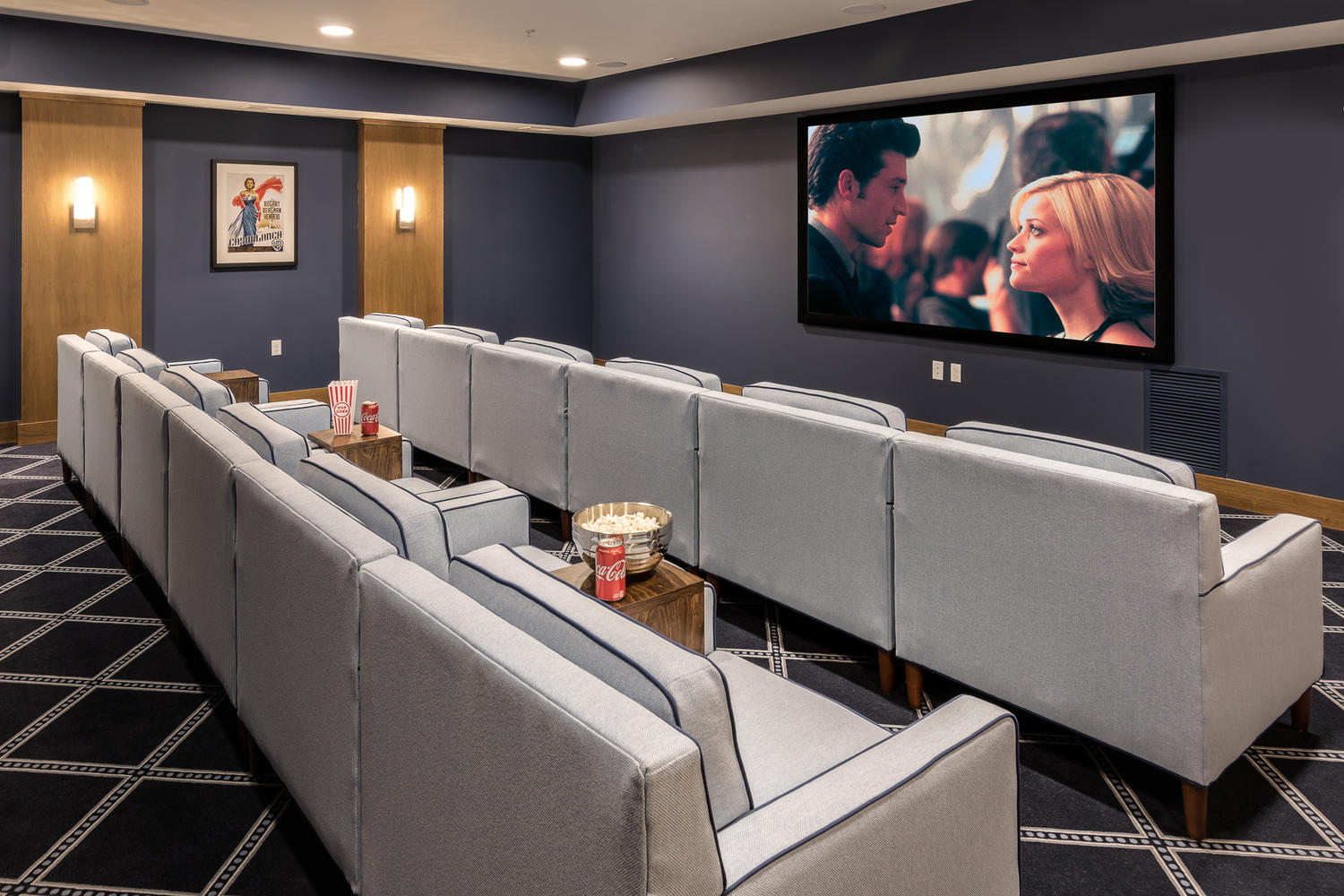 Two lines of gray chairs sitting in front of a tv on the wall. There are snacks sitting on stands next to each chair.