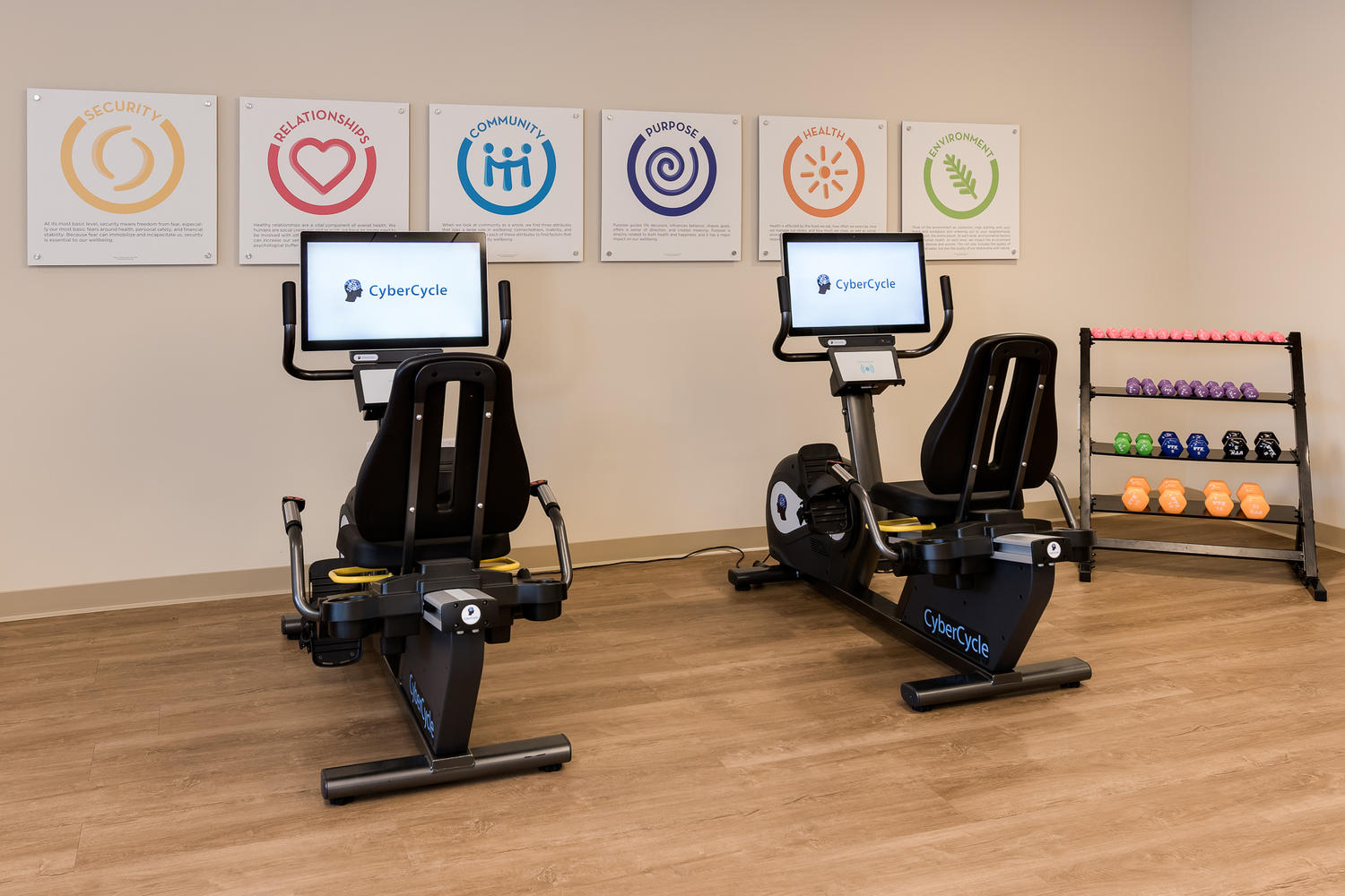 Exercise bikes on a wooden floor, with a white wall in front of them, and motivational pictures on the wall.
