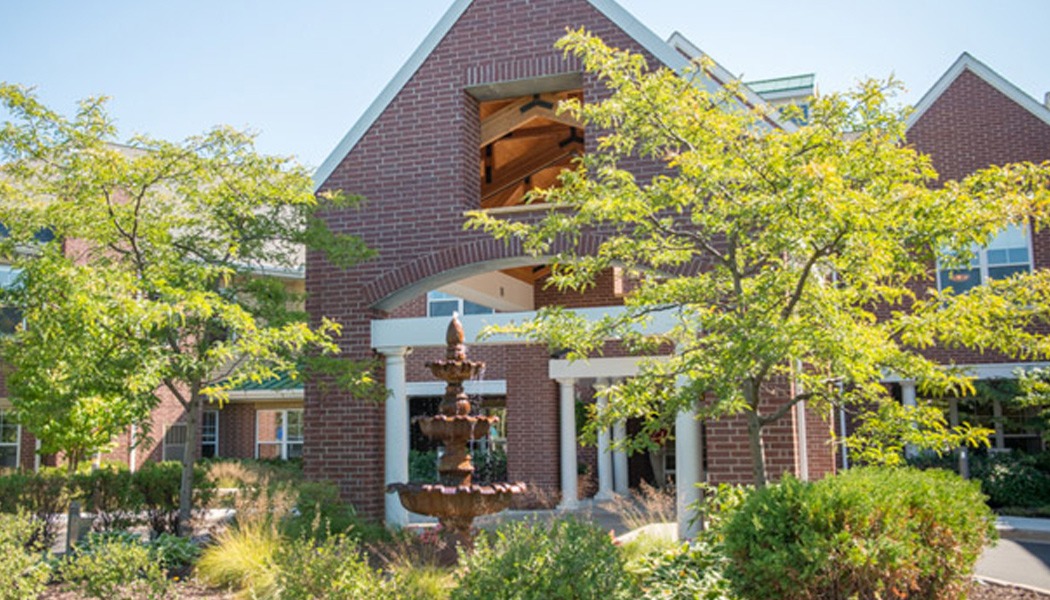 The outside of a brick building, with a fountain and some trees sitting in front of it