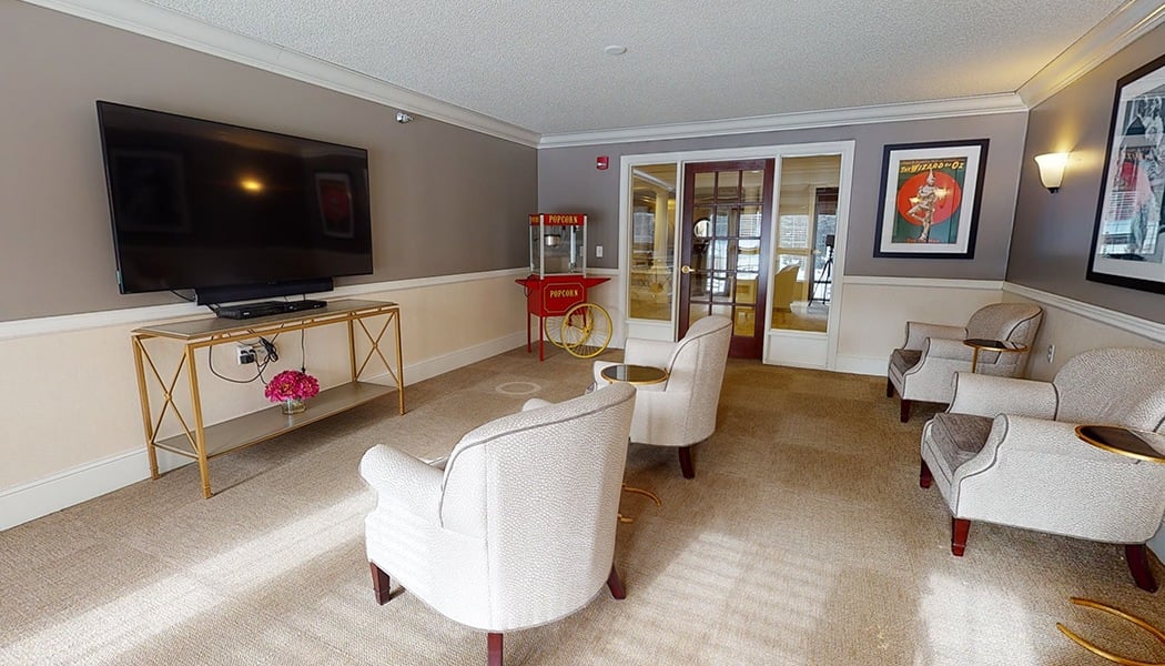 Four white chairs sitting in front of a flat-screen tv, with a popcorn machine in the corner.