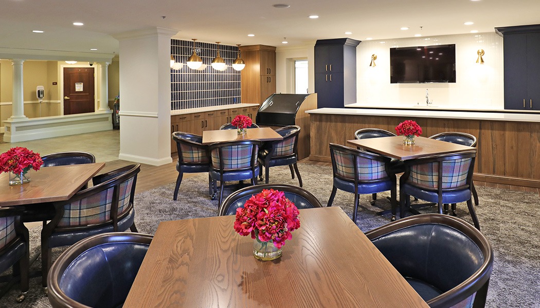 A dining room with many wooden tables, with chairs sitting around them, and a red bouquet of flowers in the center of each table.