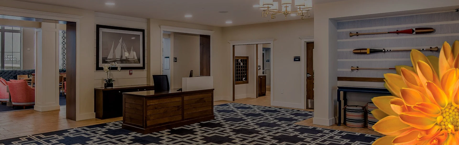 Lobby of a building with a picture of a boat and some boat oars hanging up on the wall. The carpet has a blue and white pattern, and the room is open and clean.