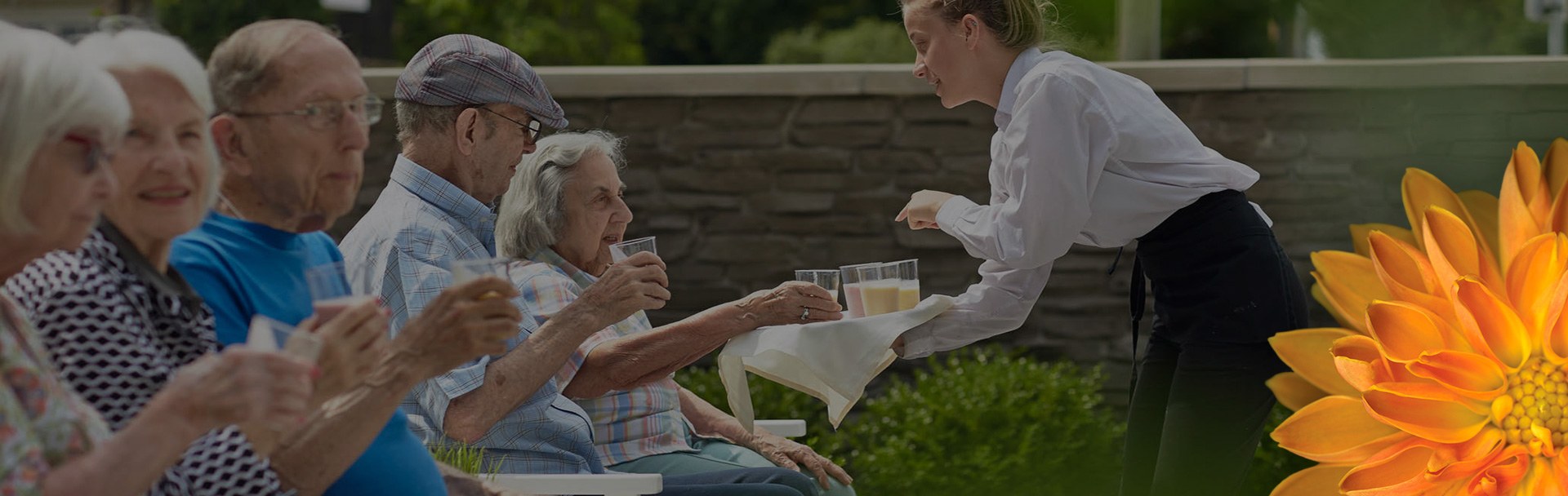 A girl handing out drinks to a group of older individuals, sitting outside on a sunny day.