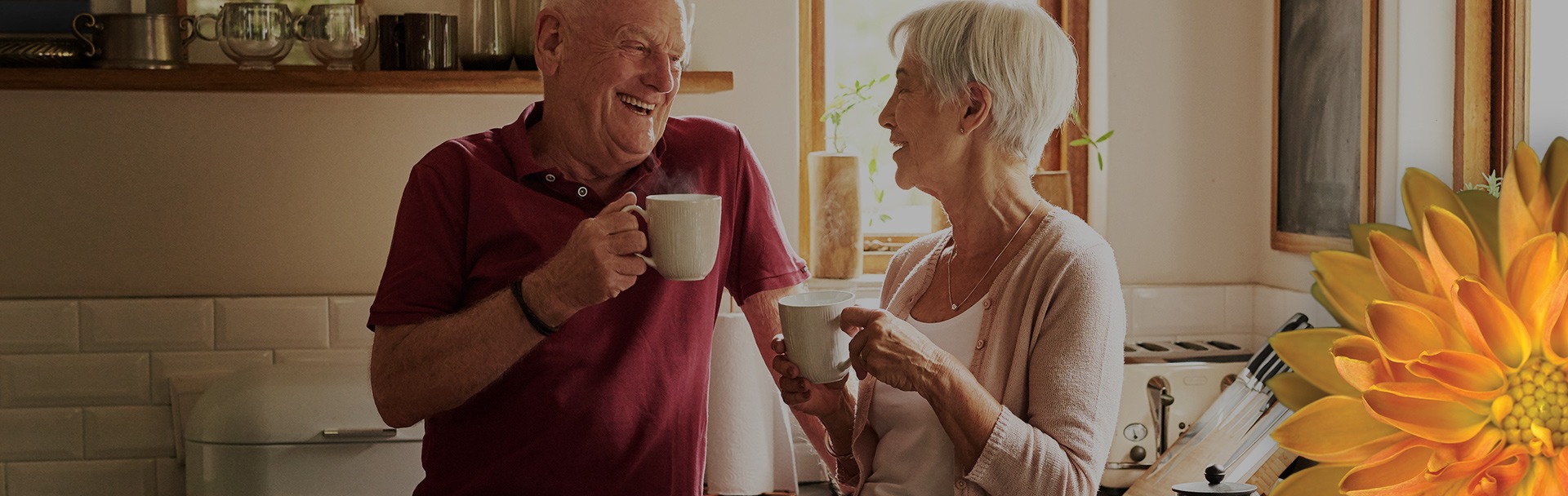 An older man and woman laughing with each other, holding a mug, in a kitchen setting