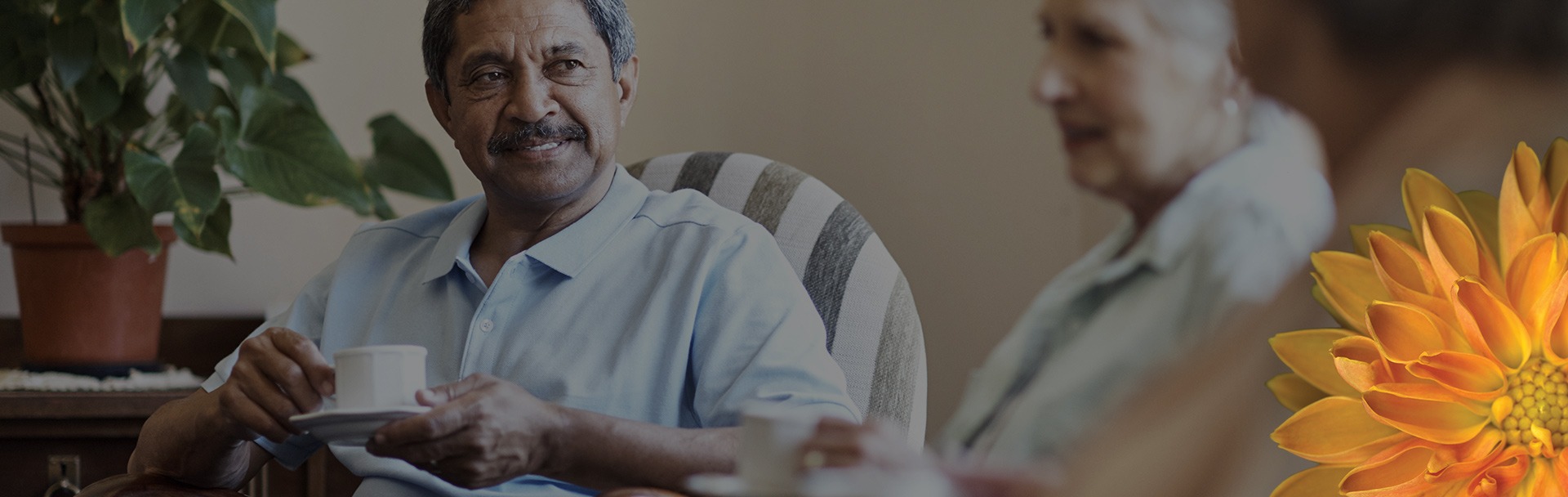 Man sitting down drinking coffee out of a mug, having a conversation with others