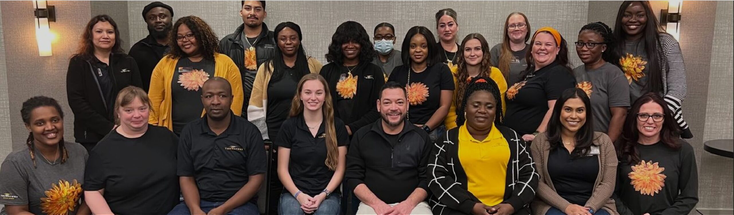 Group of diverse employees posing for a photo wearing shirts with dahlia designs.