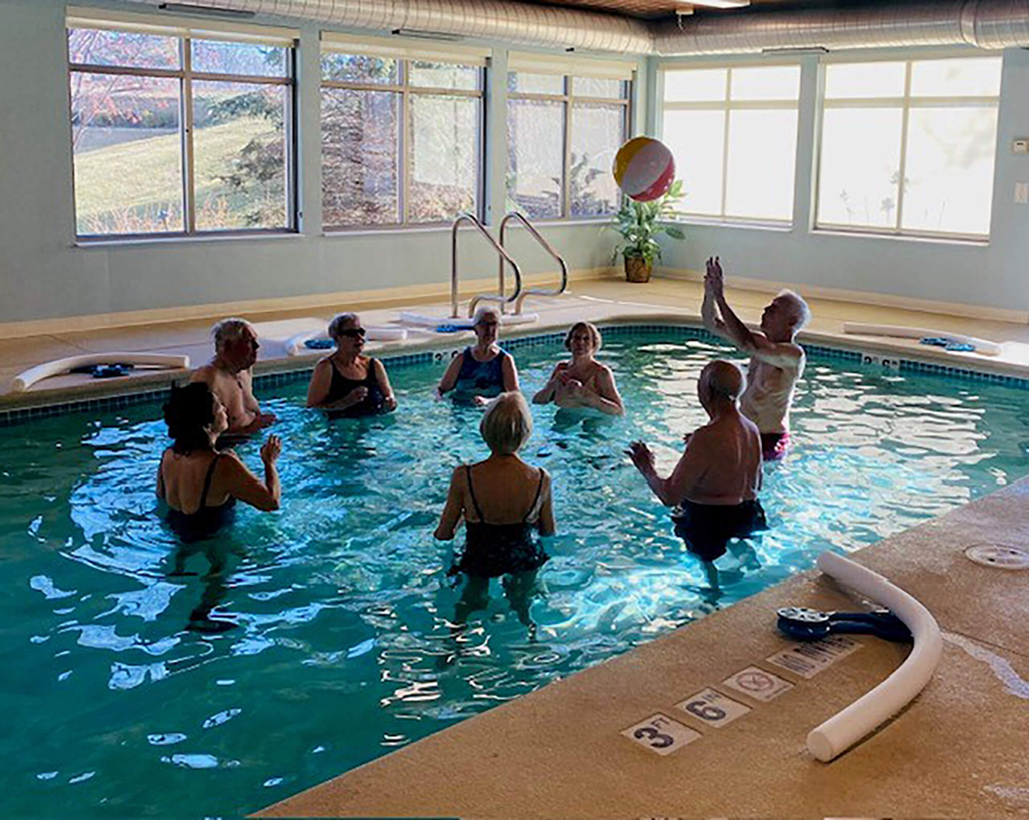Seniors participate in an aquatic fitness class in Edina, enhancing their health in a sunlit pool area with exercise equipment nearby.