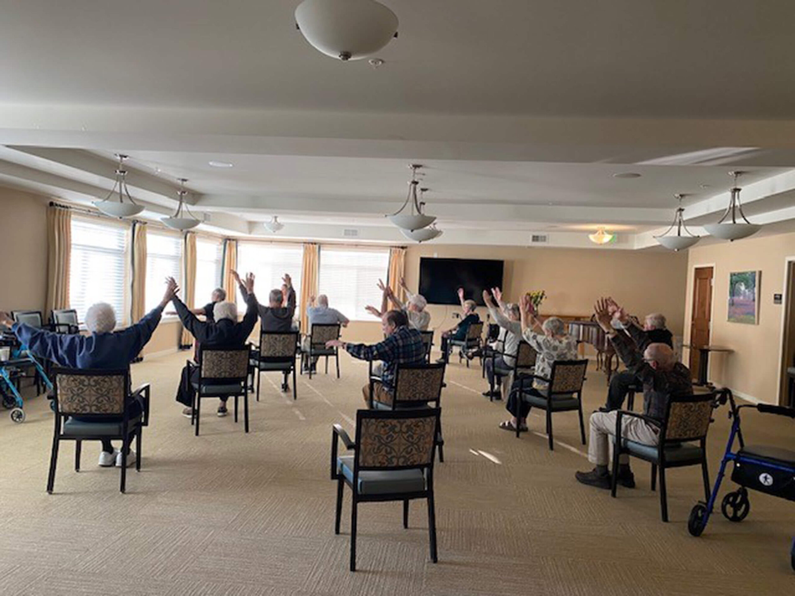 Elderly residents raising hands joyfully in a group exercise session in Edina community.