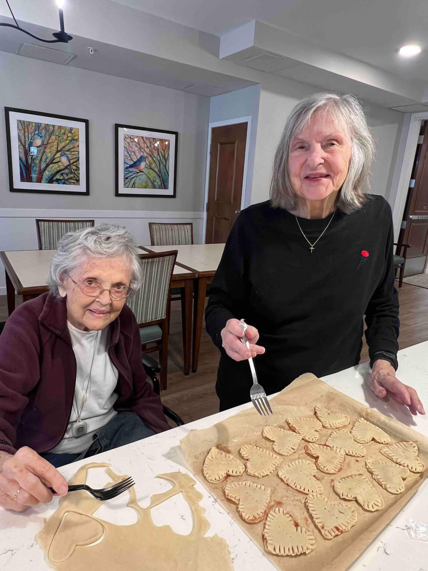 Two senior women smiling while making heart-shaped pies at an Edina living facility.