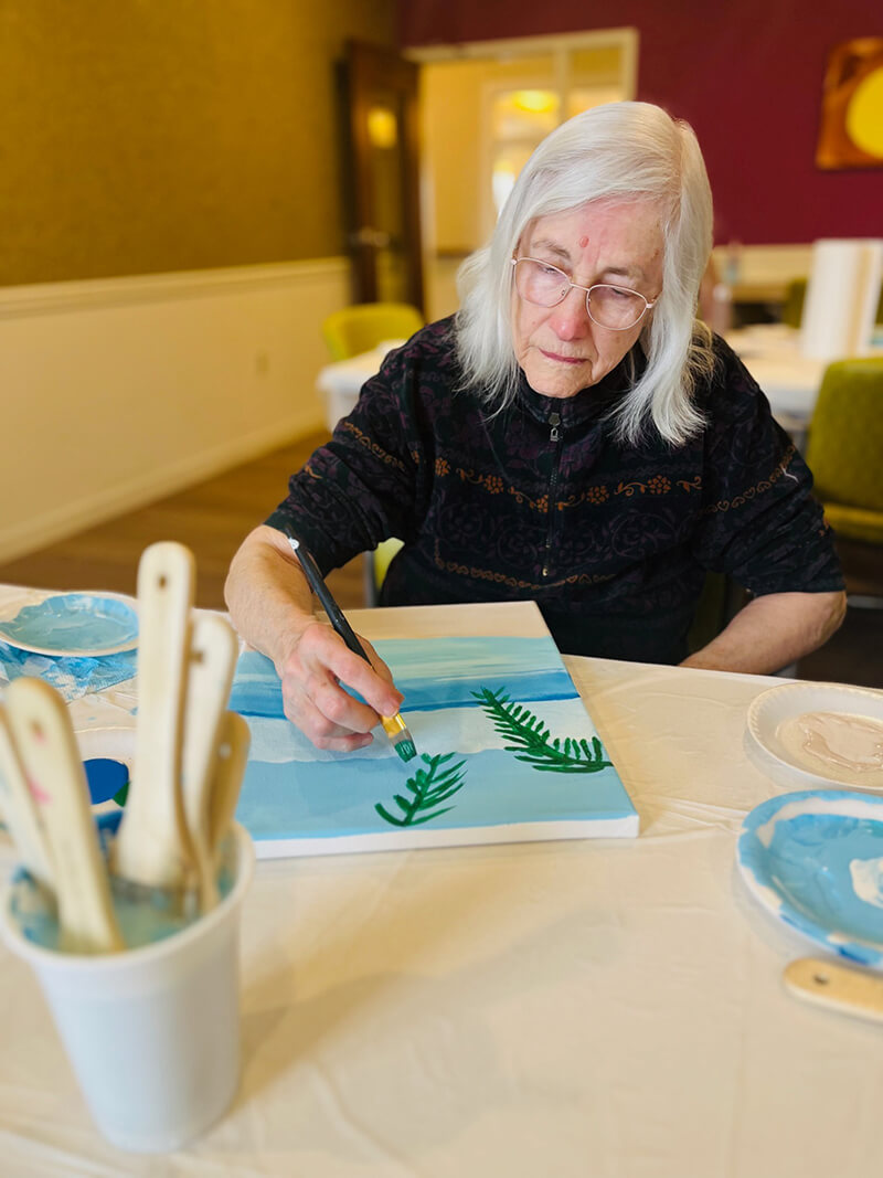 Elderly woman painting in an art class at The Waters of Highland Park.