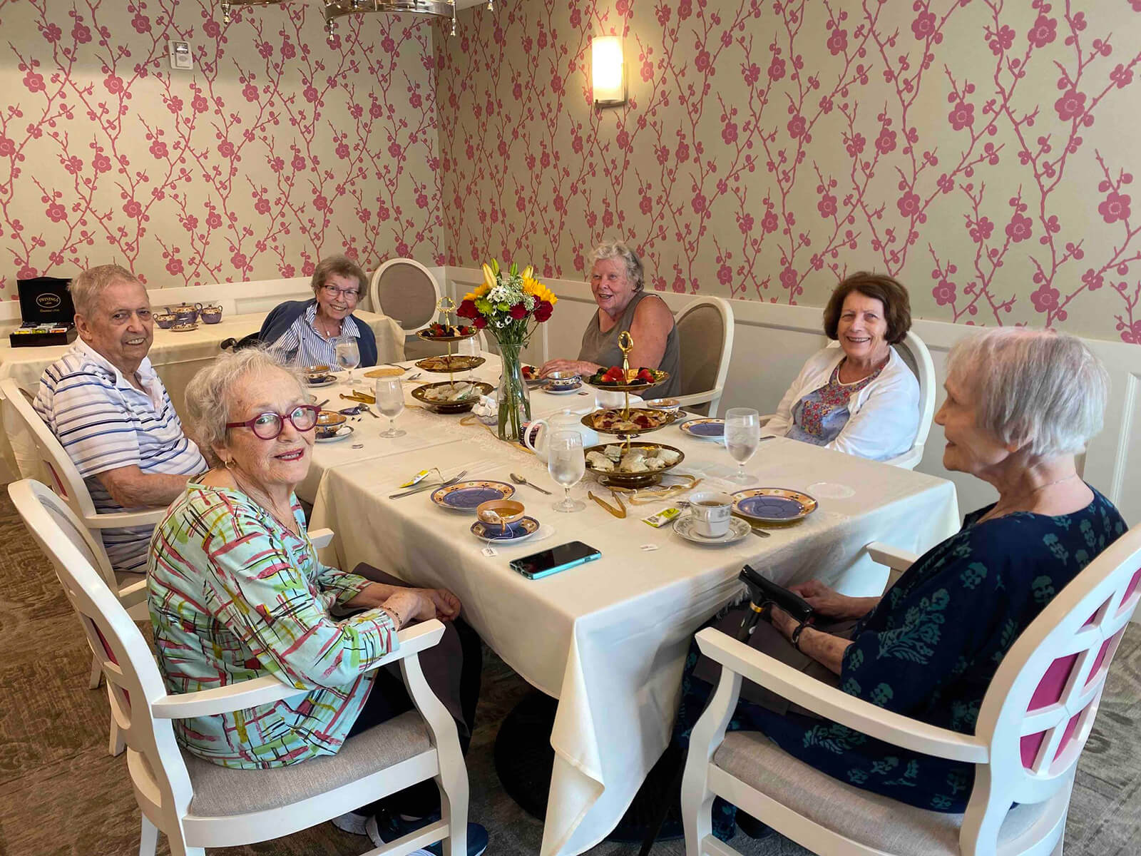 A group of seniors smiling around a dining table adorned with flowers at The Waters on 50th in Minneapolis, enjoying a communal meal.