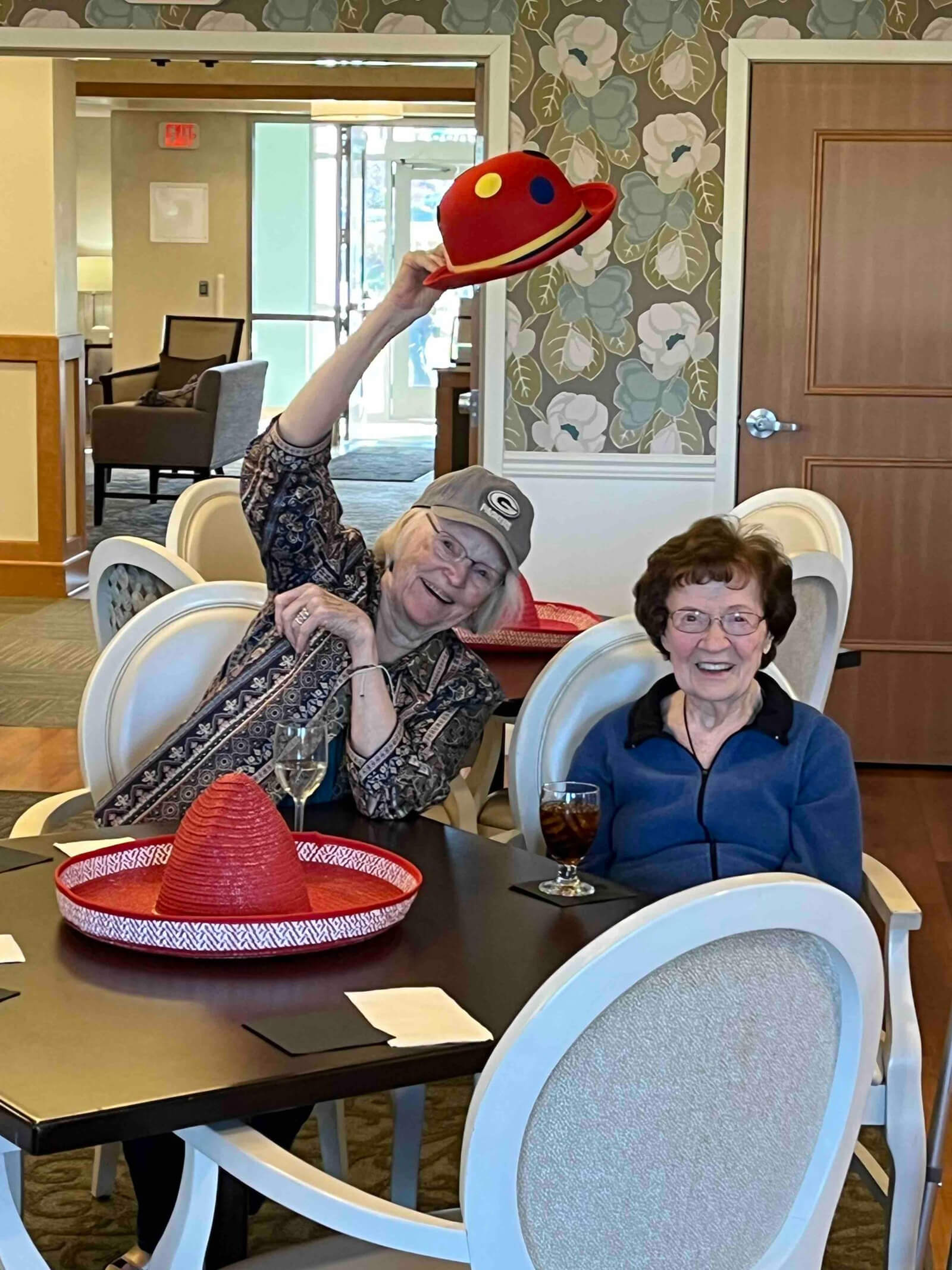 A senior resident playfully tipping a whimsical hat during a social event at The Waters of Oakdale, showcasing the joyful community atmosphere.
