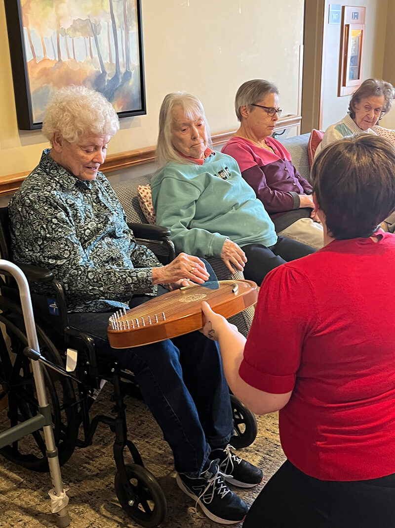 A group of residents enjoying musical therapy with a lap harp at The Waters of Plymouth.