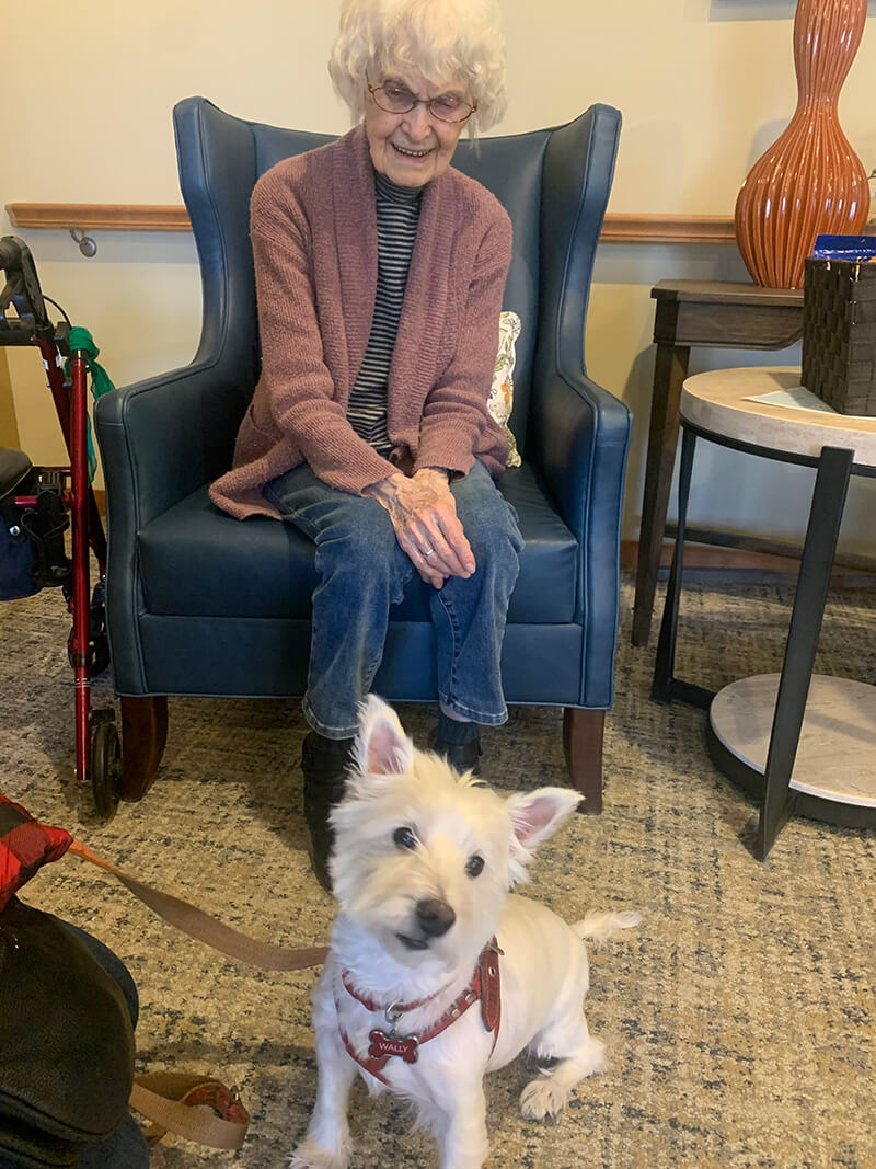 Elderly resident with a smile, petting a small dog at The Waters of Plymouth.