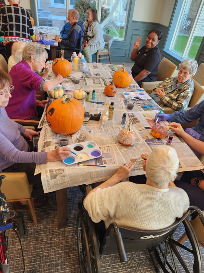 Senior residents of The Waters of Pewaukee engaging in pumpkin painting, adding a touch of color and fun to the Halloween festivities.