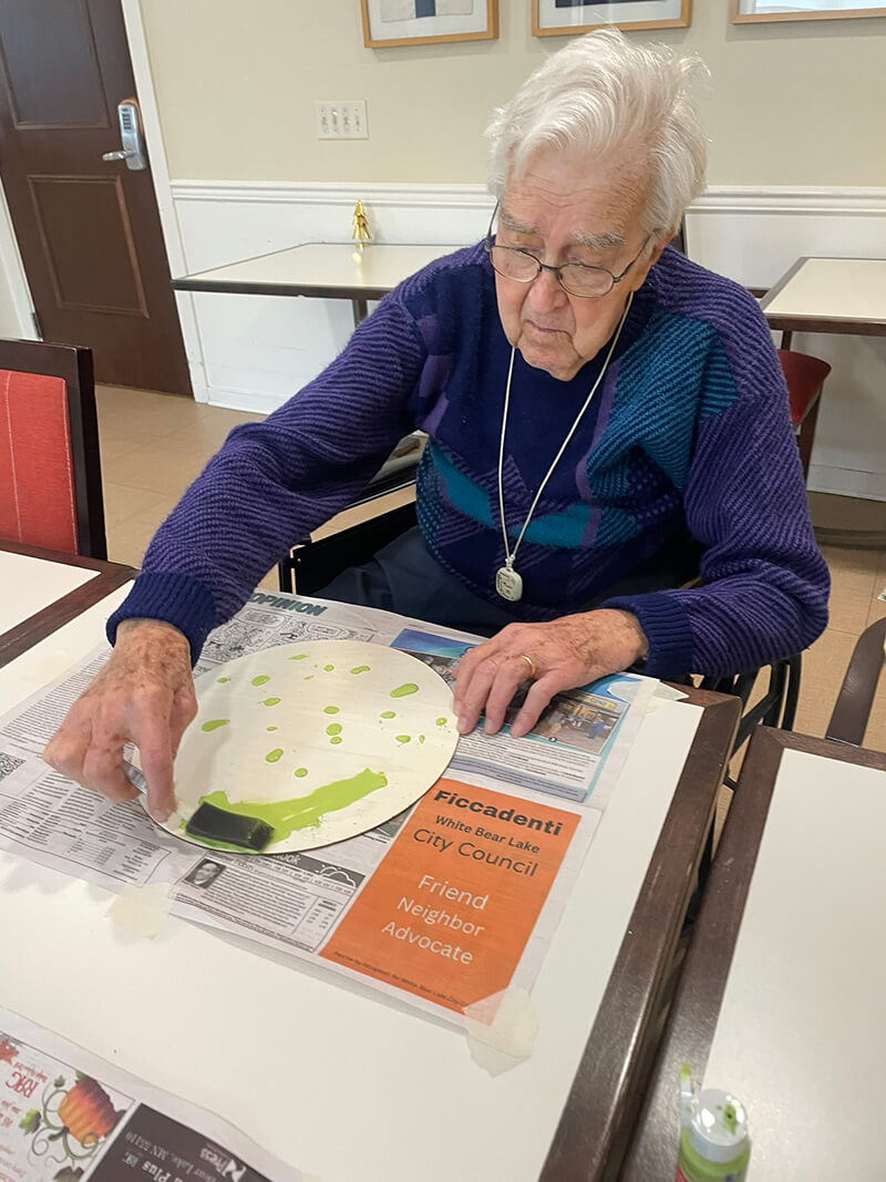 Elderly resident participating in a creative art session, crafting with paint at The Waters of White Bear Lake.