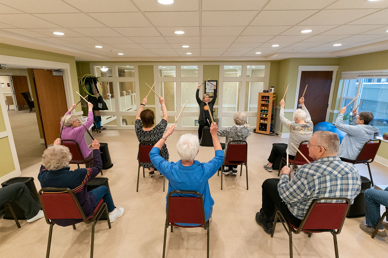 Residents of The Waters on Mayowood participating in a group exercise class with wooden sticks, promoting active senior living.