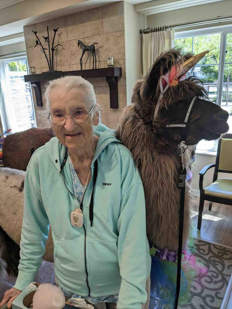 A senior resident at The Waters on 50th posing with a therapy llama, showcasing the unique wellness activities available.