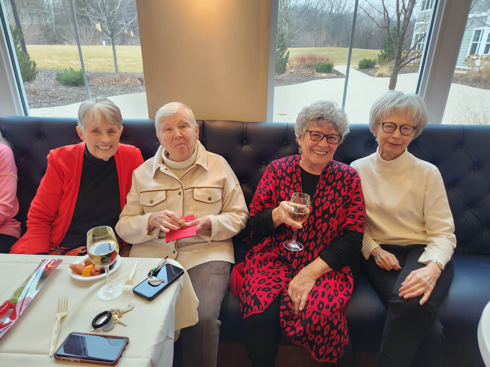 A group of joyful seniors at The Waters of Excelsior sharing stories and toasting with glasses of wine during a social gathering.